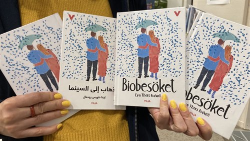 Person håller upp fyra exemplar av samma bok fast på olika språk.
