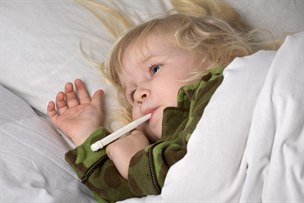 Barn ligger i sängen med termometer i munnen