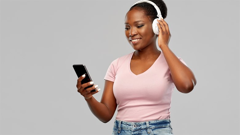 En tjej lyssnar på något i vita hörlurar via mobilen.
