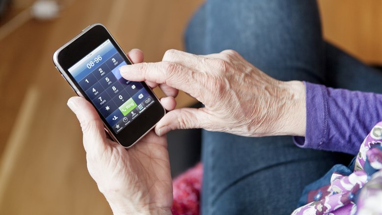 En äldre person slår ett nummer på sin mobil.