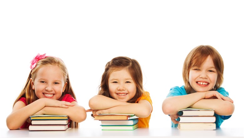 Tre barn lutar sig mot en liten stapel med böcker var, tittar in i kameran och ler.