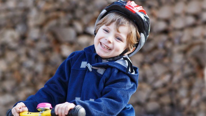 Pojke med hjälm cyklar och ler